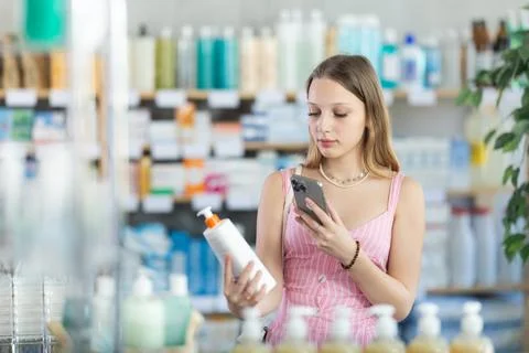 Girl in summer clothes scans code on package of cream to check expiration date Stock-Fotos