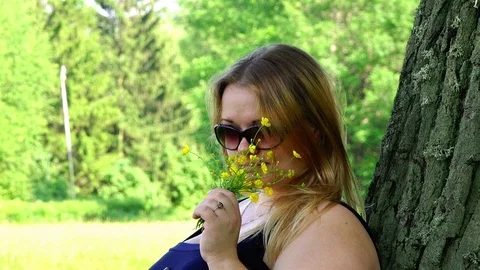 A girl in sunglasses in the fresh air inhales the fragrance of wild flowers in Stock Footage