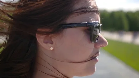 Girl in sunglasses posing in front of camera, hair developing in the wind. slow Stock Footage 78537047