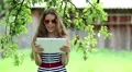 Girl in sunglasses with tablet pc stands under the tree in garden HD Footage