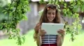 Girl in sunglasses with white tablet pc stands under apple tree in garden HD Footage