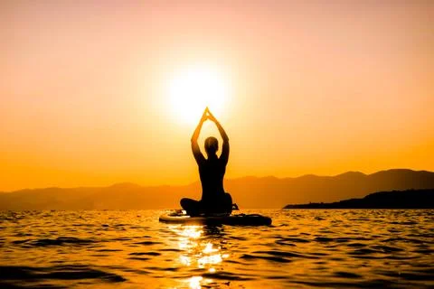 Girl at sunset on a paddleboard is engaged in yoga. hands up at Stock Photos