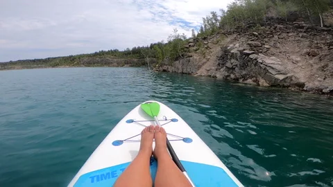 Girl SUP board floating surface blue water quarry lake with rocky shores trees Stock Footage 284243752