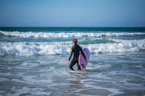 Girl with a surfboard overcomes the waves Stock Photos