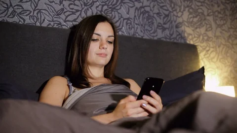 Girl surfing internet while lying in bed in the bedroom at night, wrote sms Stock Footage 98201659