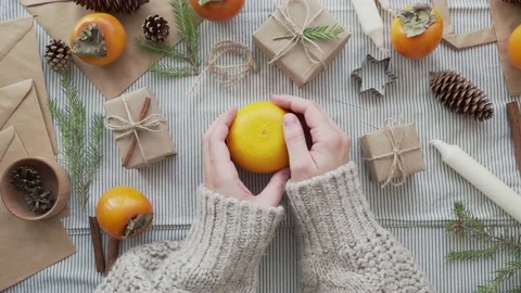 A girl in sweater holds a tangerine in her hands, surrounded by Christmas gifts Stock Footage