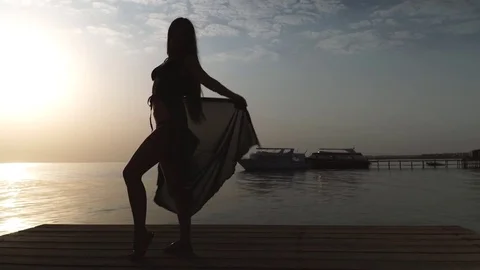 A girl in a swimsuit and a cloak is standing on the pier and meets the dawn Stock Footage