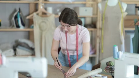 Girl tailor draws pattern on a sheet of paper in a sewing workshop Stock Footage 310532806