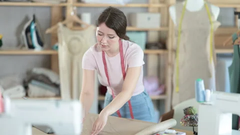 Girl tailor draws pattern on a sheet of paper in a sewing workshop Stock Footage 319494100