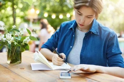 Girl taking notes using smartphone. Outdoor portrait of a young woman writing in Stock Photos