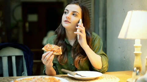 Girl talking on cellphone while eating pizza in the cafe Stock-Footage 62387565