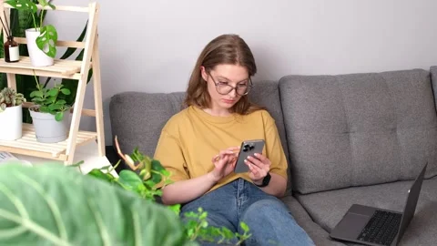 Girl talking on phone while sitting on the sofa surrounded by indoor plants. Stock Footage 274499872