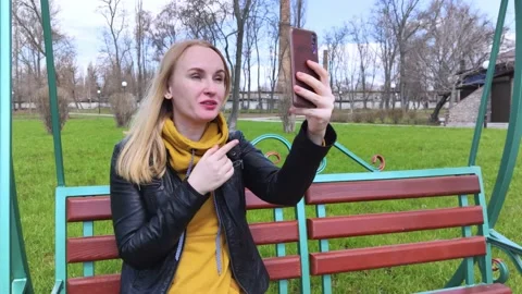 The girl is talking by video communication while sitting on a swing in the park. Stock Footage 152234679