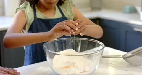 Girl tapping egg on bowl, cracking and adding yolk to flour for mixing, parent Stock Footage 335514202