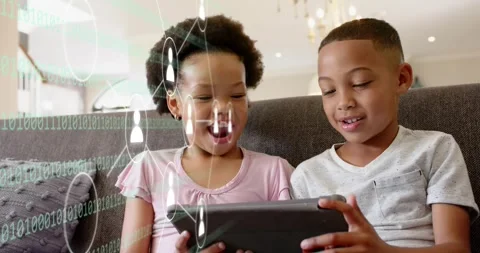 Girl tapping tablet on couch as binary overlay from left, boy sharing control Stock Footage 321363014