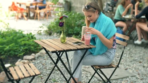 Girl texting on smartphone and drinking cocktail in the outdoor cafe Stock Footage
