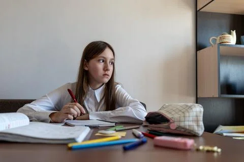 Girl thinking about school problem at table and writing solution in notebook. Stock Photos