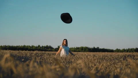 A girl throws a black hat in front of her standing in a wheat field at sunset Stock Footage 204960068
