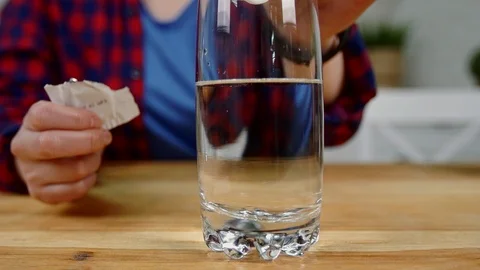 Girl throws effervescent tablet into glass of water at table Stock Footage 101249491