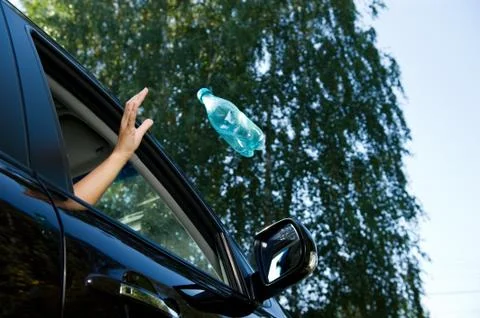 A girl throws an empty plastic bottle into the open window of a car. A flying Stock Photos