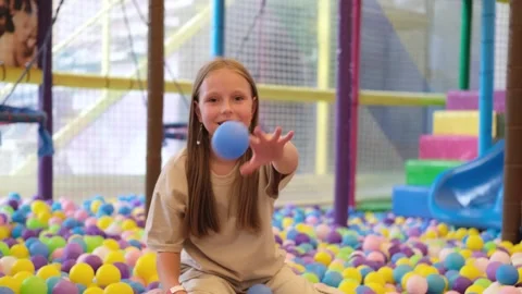 Girl throws multi colored plastic balls in big dry paddling pool Stock Footage 255925092