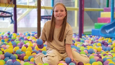Girl throws multi colored plastic balls in big dry paddling pool Stock Footage 255925178