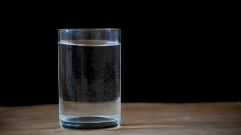 The girl throws a white effervescent tablet into a glass of water on the table. Stock Footage 103168550