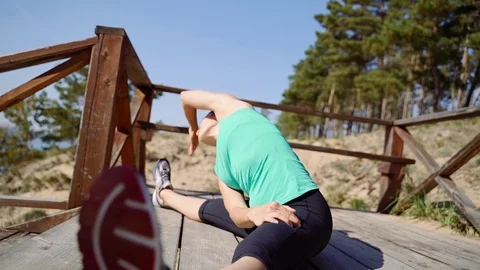Girl tilts to the side while sitting on a wooden floor. Training in the open air Stock Footage 123102143