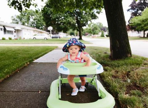 A girl, toddler, walking through a suburban neighborhood using a walking fram Stock Photos