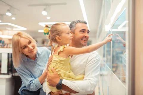 Girl touching window while looking at parrots with parents Foto stock