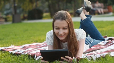 Girl with Touchscreen Tablet Lying on Grass in Sunny Lights Video stock 65500381