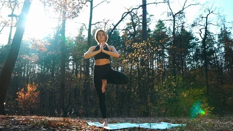 Girl in tracksuit does tree position on mat in autumn forest Stock Footage 125270438