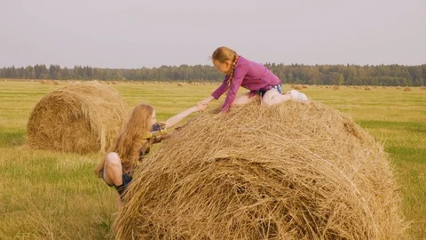 Girl is trying to climb on hay stack to friend sitting on top and helping her. Vidéo 114261207