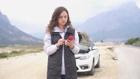 A girl is trying to solve a problem with a broken car using her mobile phone. Video stock 168985041