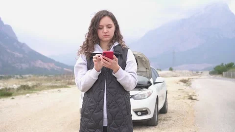 A girl is trying to solve a problems with a broken car using her phone. Stock Footage 168984970