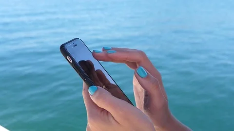 Girl type slide use mobile phone chatting on blue sea water background Greece Stock Footage