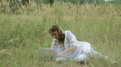 Girl typing on a computer in a field Stock Footage 12412079