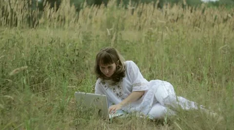 Girl typing on a computer in a field Stock Footage 12412118