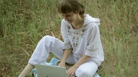 Girl typing on a computer in a field Stock Footage 12412440