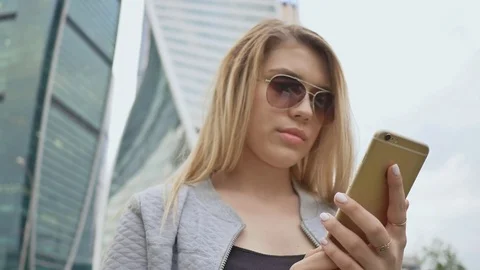 Girl typing on a phone against the background of high-rise buildings in the Stock Footage