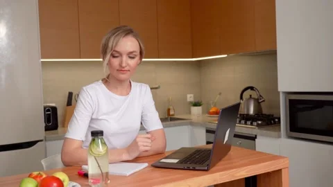 The girl is typing text on a laptop while sitting at the table in the kitchen Stock Footage 154797293