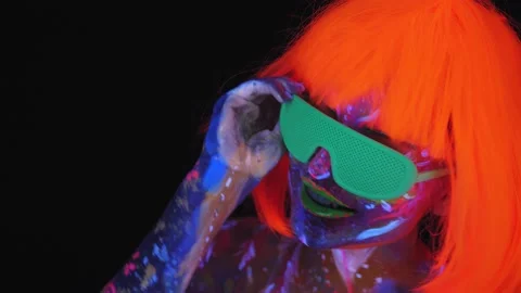 A girl with an ultraviolet pattern on face in an orange wig dances in the dark Stock Footage 146127264