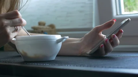 Girl uses her smartphone while she's having breakfast Stock Footage 79024740