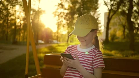 Girl uses smart phone while sitting on swing outdoors on sunset, slow motion Stock Footage 239019792