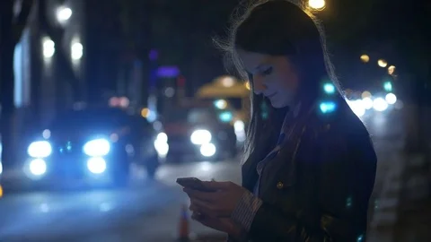Girl uses a smartphone against cars moving on a night street Stock Footage