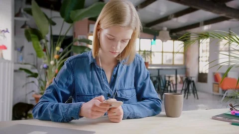Girl using app on mobile phone drinking coffee in headphones listening to music Stock Footage 103286234