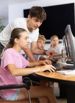 Girl using computer and teacher helping to him in classroom 库存照片