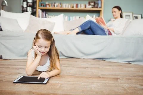Girl using digital tablet with mother reading book Stock Photos