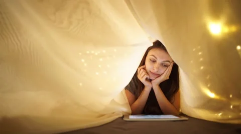 Girl using digital tablet under blanket while lying on bed at home Stock Footage 56317202