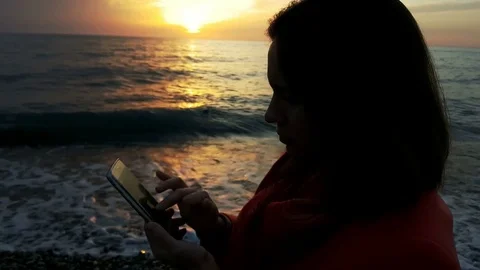 The girl is using her mobile at the sunset at the coast Stock Footage 83960476